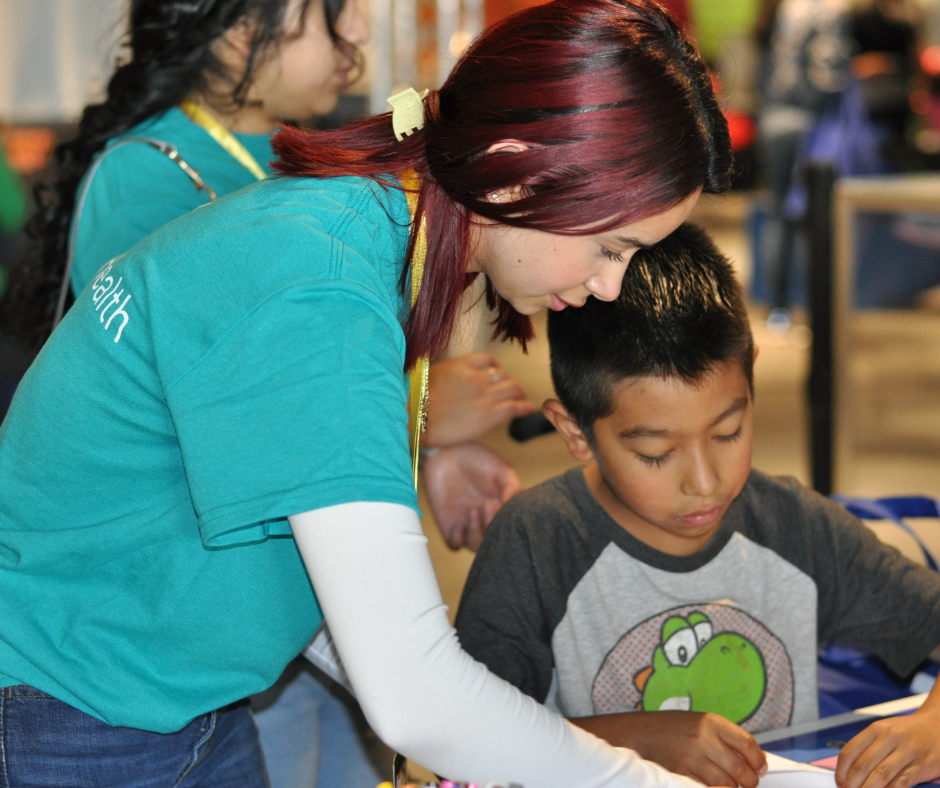 Teen volunteer helping a child fold a paper airplane at the Monroe Science Center